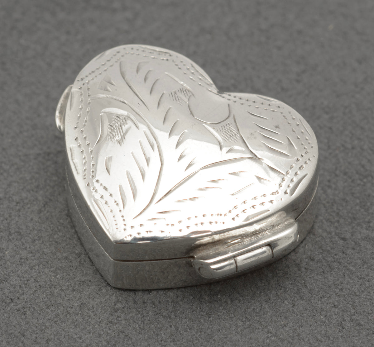 Engraved foliate lid and dotted heart outline on the silver box against a grey background