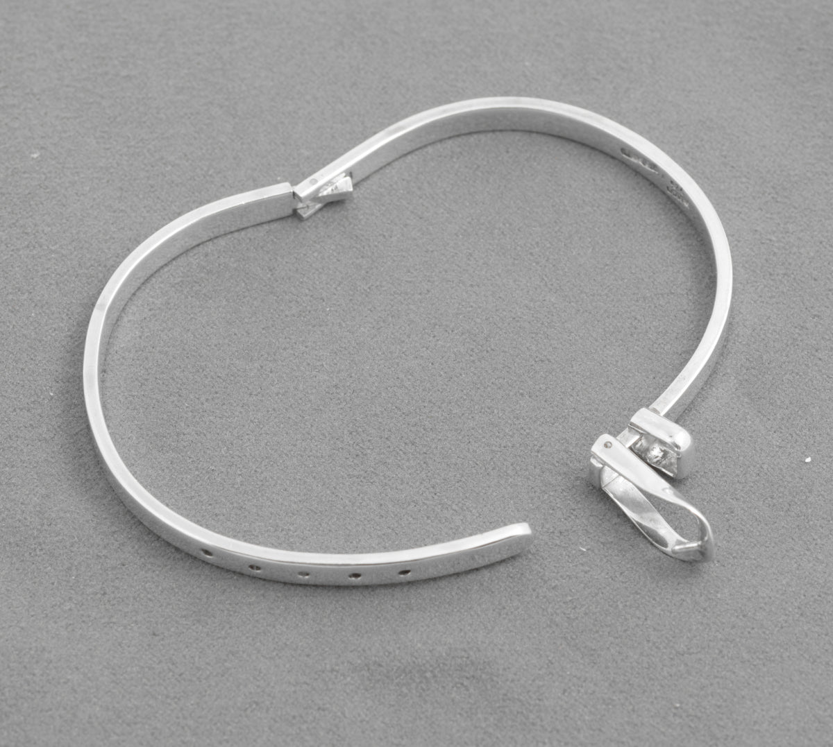 Silver belt bangle open with hinged buckle raised and five adjustment holes visible