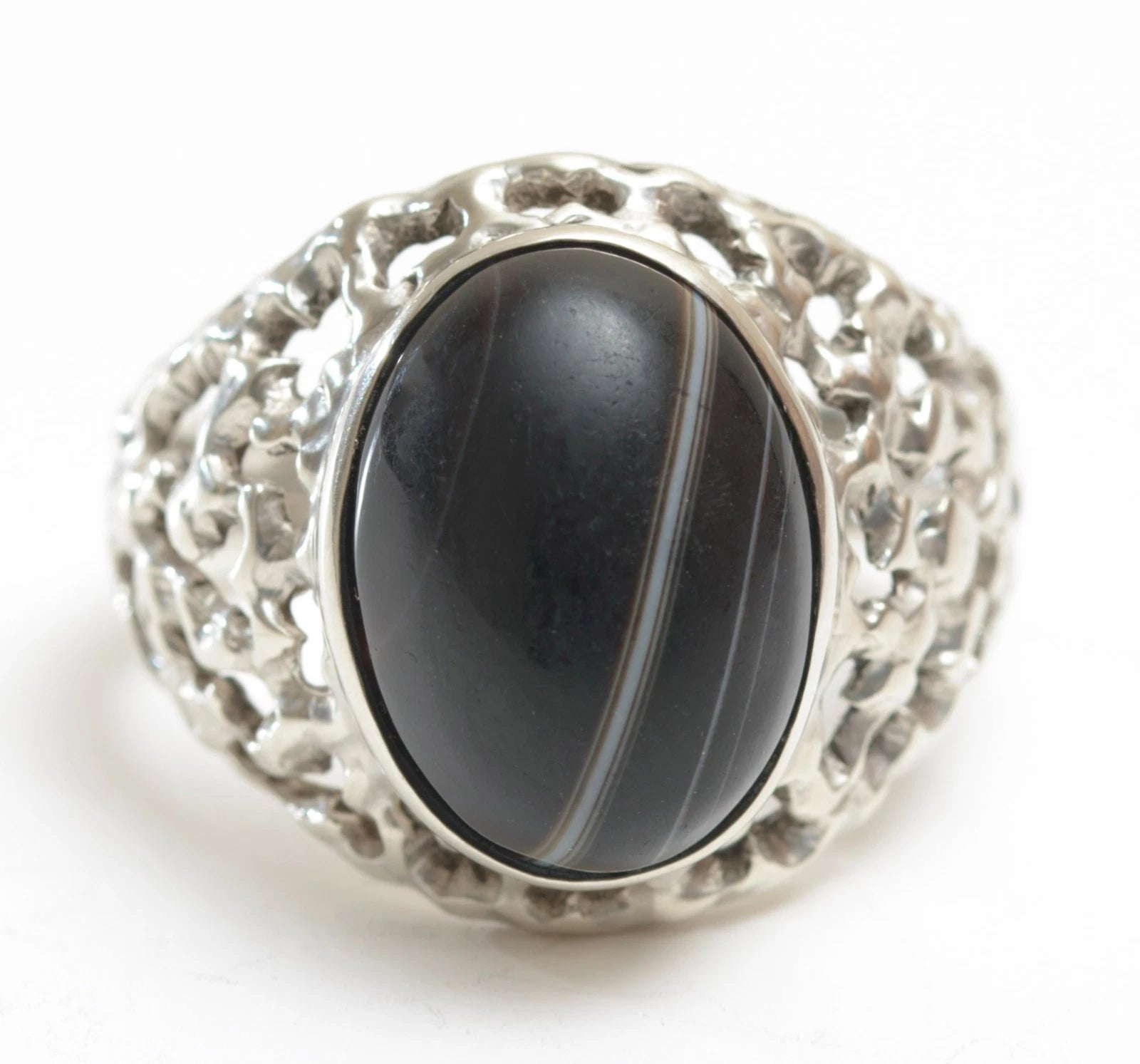 A vintage sterling silver brutalist statement ring from the 1970s, bezel set with a semi-polished oval banded agate cabochon in deep charcoal, black, grey, and cream tones.